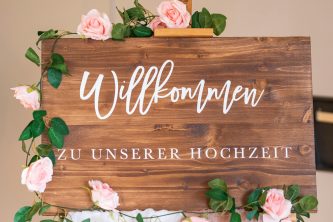 Wooden welcome sign adorned with pink roses for a wedding celebration.